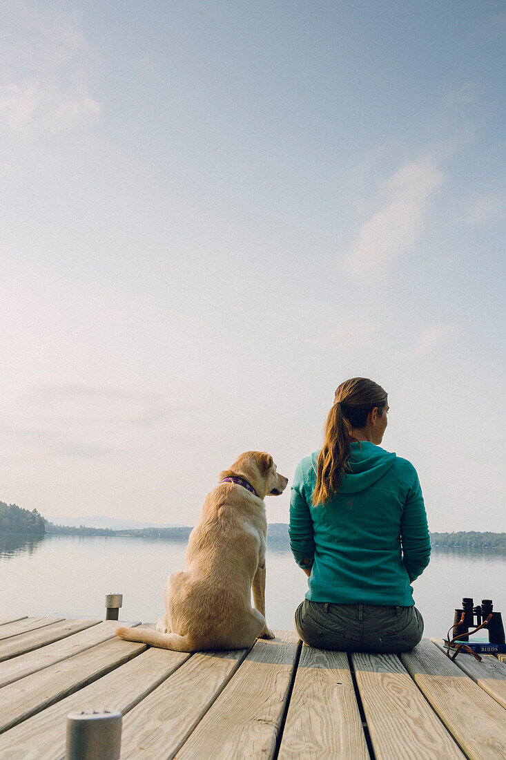 Rear View Of Woman And Dog Sitting On Edge Of Dock In Caspian Lake