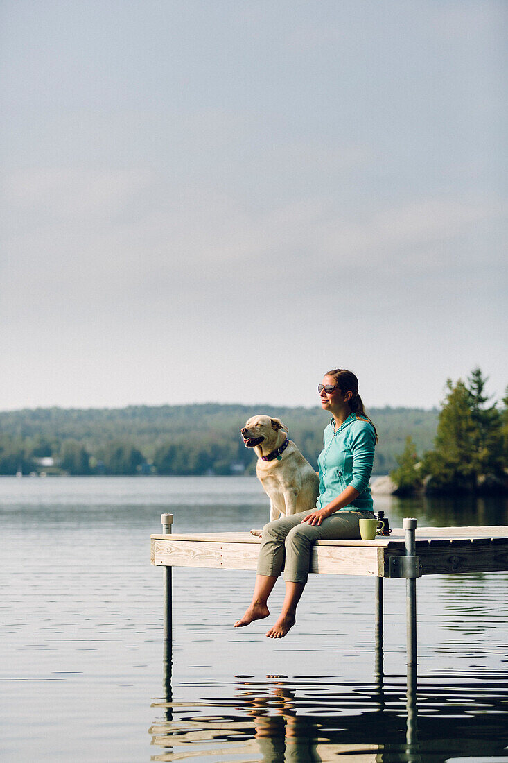 Woman And Dog Sitting On The Edge Of Dock On Caspian Lake