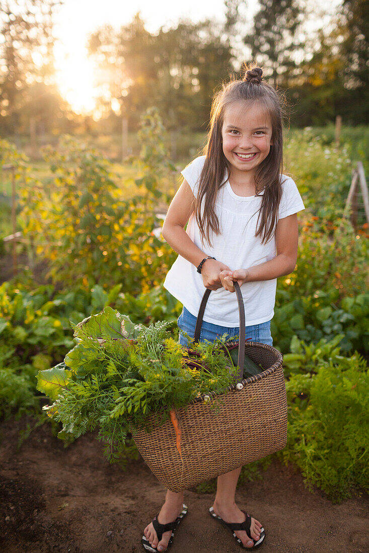 A Young Girl Holding A Basket Full Of Vegetables Standing In The Garden
