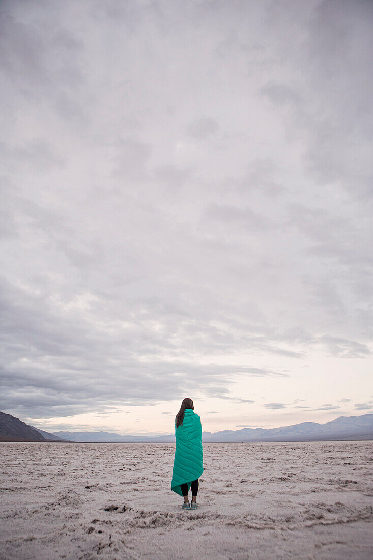 A Woman Wrapped In A Blanket Looking At Sunrise From Badwater Basin, Death Valley National Park, California