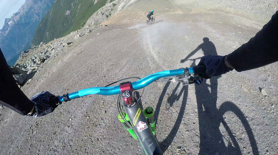 POV past hands of mountain biker in descent from mountain ridge