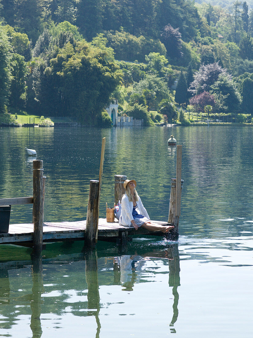 Mature woman dips feet in lake at end of dock