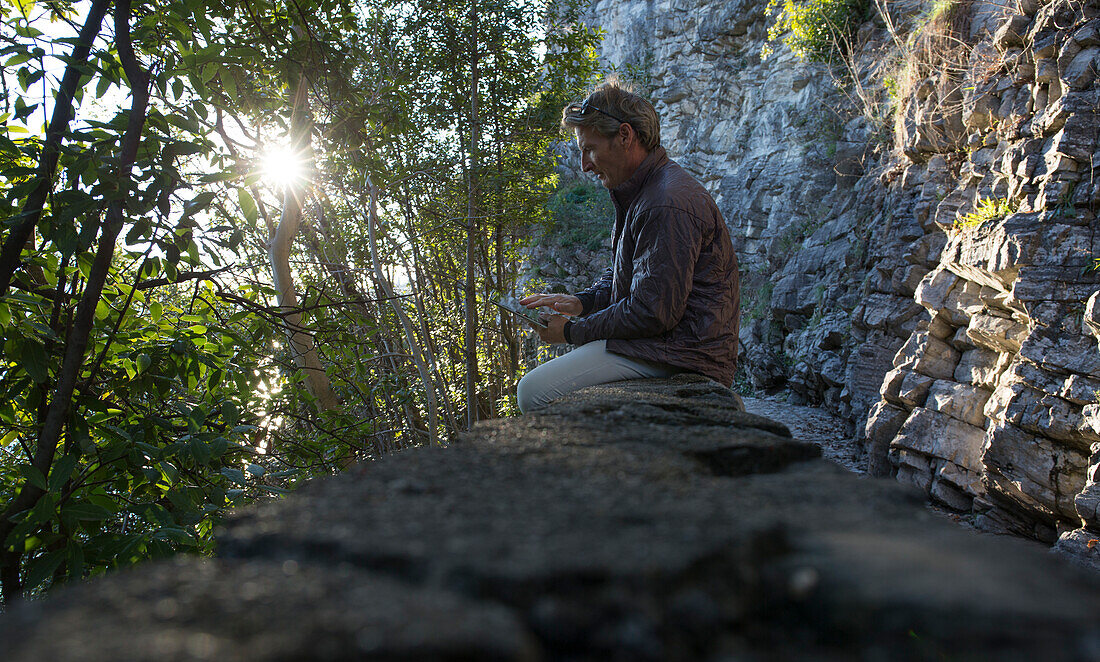 Man checks tablet on rock wall along path