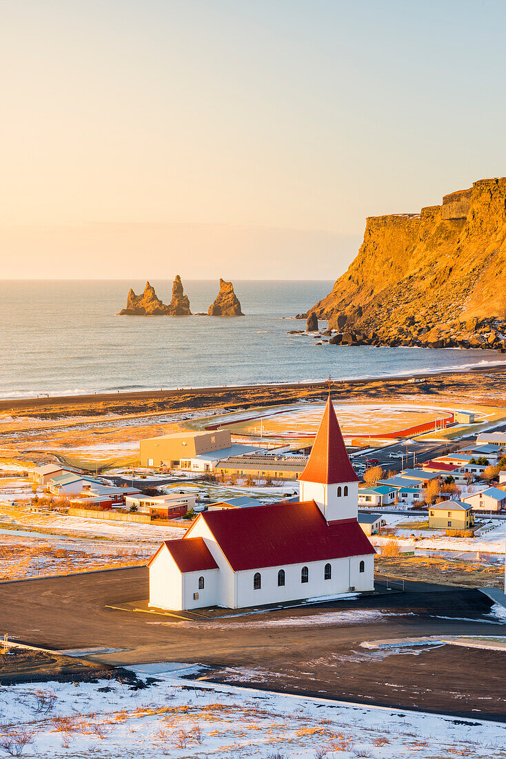 Vik i Myrdal, Süd-Island, Island, Erhöhte Ansicht über Viks Kirche, das Dorf und die Reynisdrangar-Felsen bei Sonnenaufgang