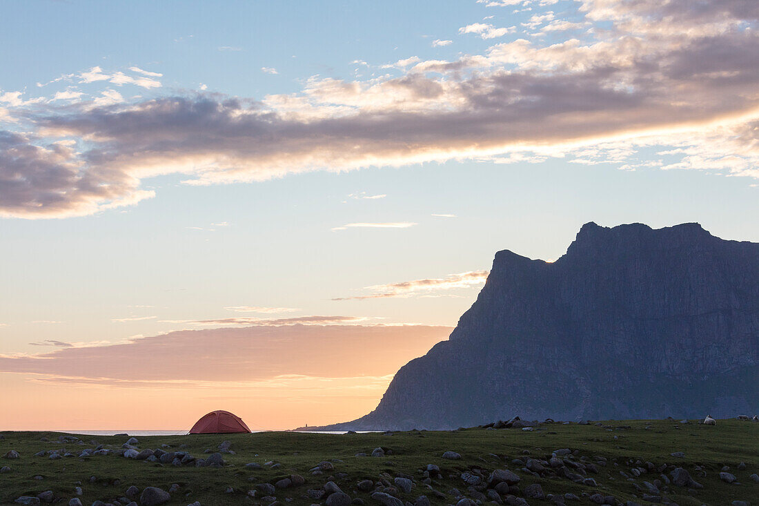 The pink sky at midnight sun lights up the tent by the sea surrounded by rocky peaks Uttakleiv Lofoten Islands Norway Europe