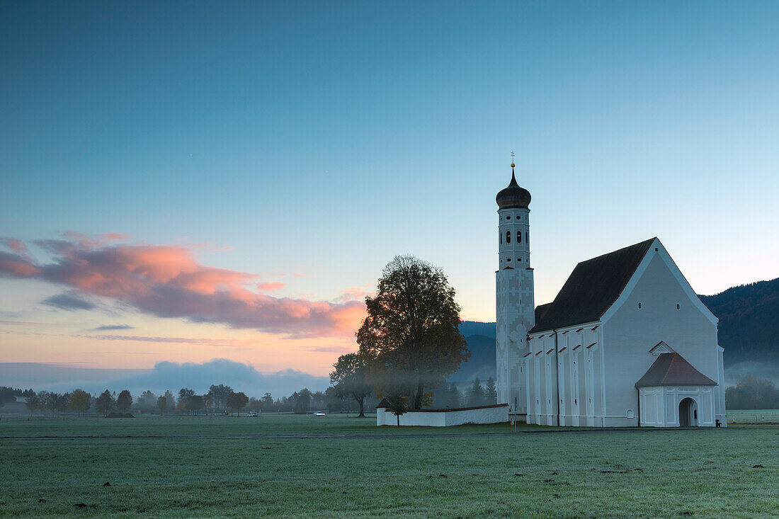 Pink clouds at sunrise on St Coloman Church surrounded by woods Schwangau Bavaria Germany Europe