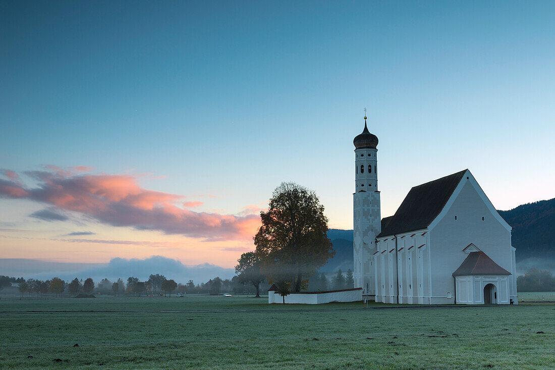 Rosa Wolken am Sonnenaufgang auf St. Coloman Kirche umgeben von Wäldern Schwangau Bayern Deutschland Europa