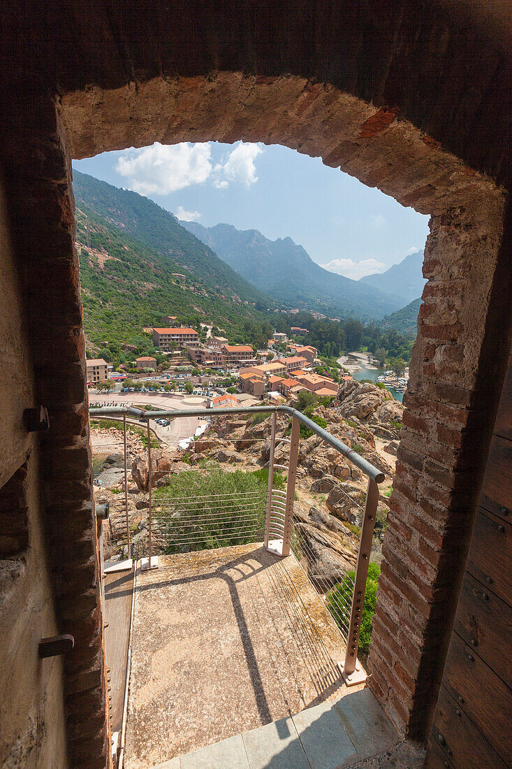 A stone arch of an old alley frames the typical village of Porto immersed in the green vegetation Southern Corsica France Europe