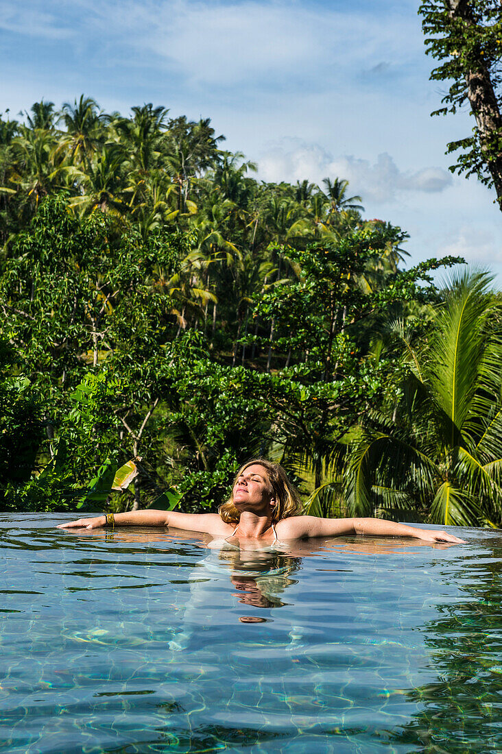 Woman enjoying an overflowing pool above a valley in the Kamandalu Ubud resort, Ubud, Bali, Indonesia, Southeast Asia, Asia