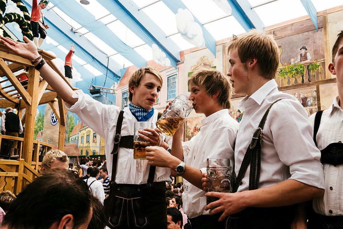 Young men in leather trousers standing on beer benches celebrate Oktoberfest in the beer tent