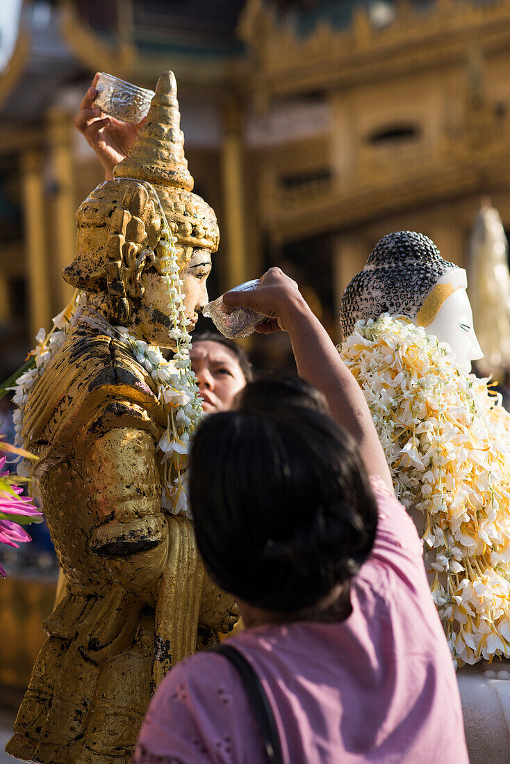 People pouring water over a Buddha statue at the Shwedagon pagoda, Yangon, Myanmar.