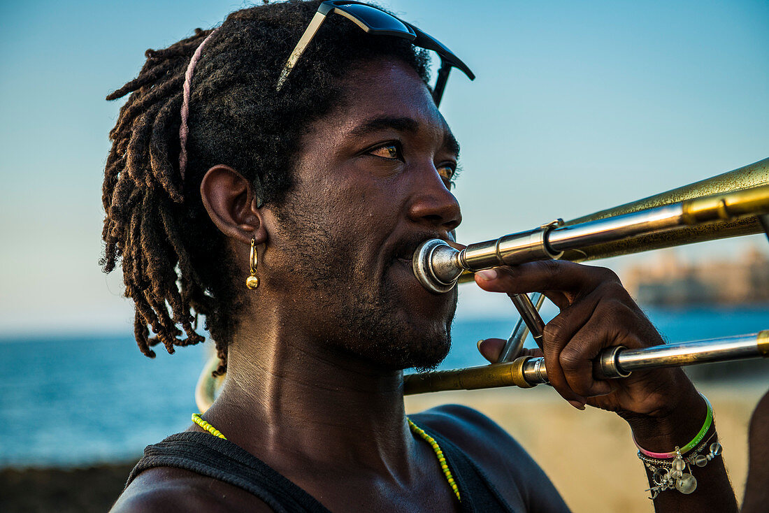 Afro Cuban man with dreadlocked hair plays trombone for tourist on the Malec??n (Avenida de Maceo), the seawall and promenade along the coast of Havana, La Habana, Cuba.