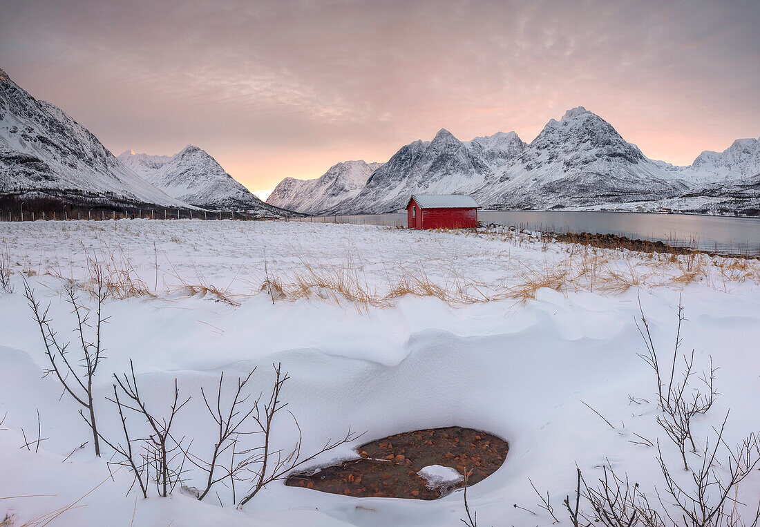 Panorama of pink sky at dawn on the wooden hut surrounded by frozen sea and snowy peaks, Svensby, Lyngen Alps, Troms, Norway, Scandinavia, Europe