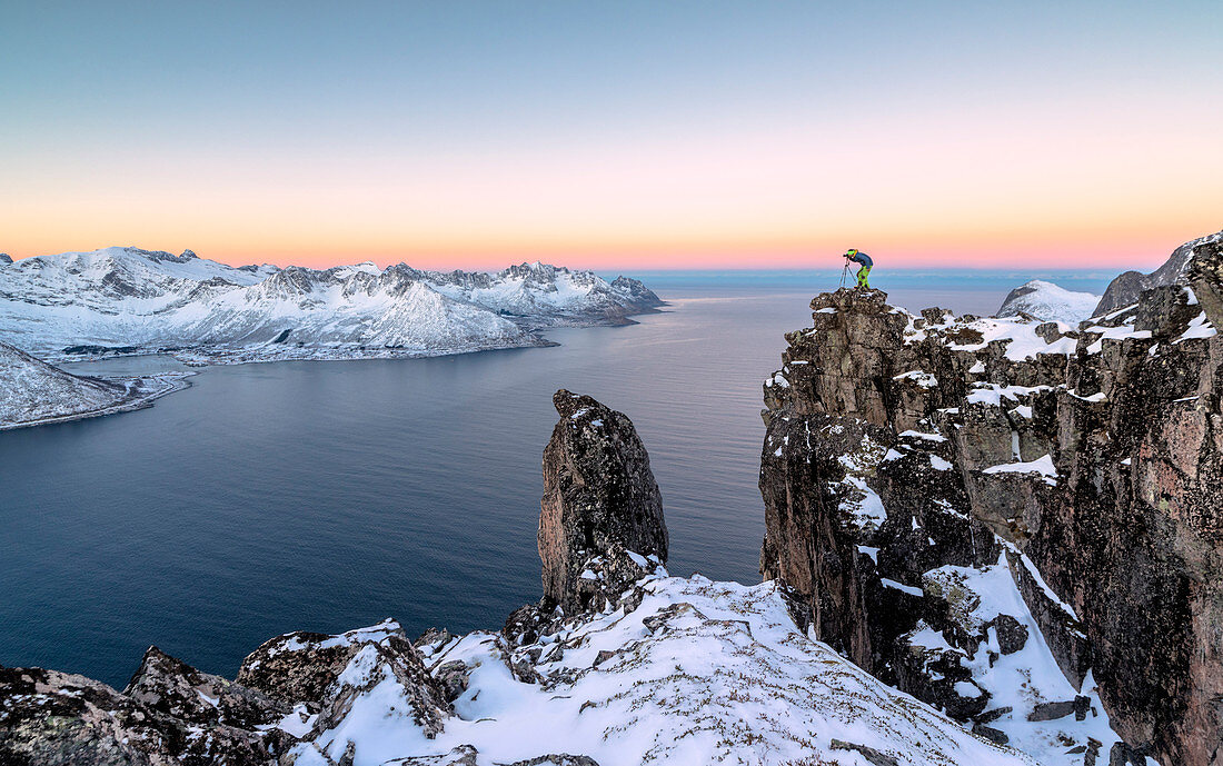Photographer on the rocks on top of Mount Hesten admires the Mefjorden and the frozen sea at sunrise, Senja, Troms, Norway, Scandinavia, Europe