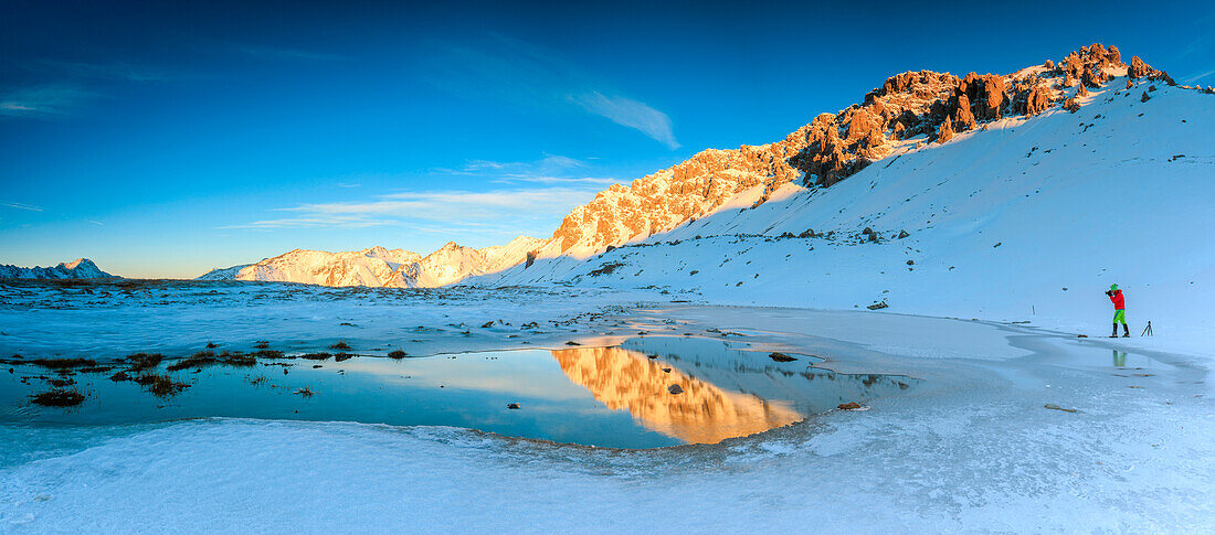 Panorama of Lake, Piz Umbrail at dawn with photographer in action framed by snow, Braulio Valley, Valtellina, Lombardy, Italy, Europe