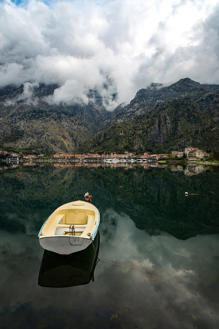 A small fishing boat sits in the reflection of the Old Town (stari grad) of Kotor in Kotor Bay, UNESCO World Heritage Site, Montenegro, Europe