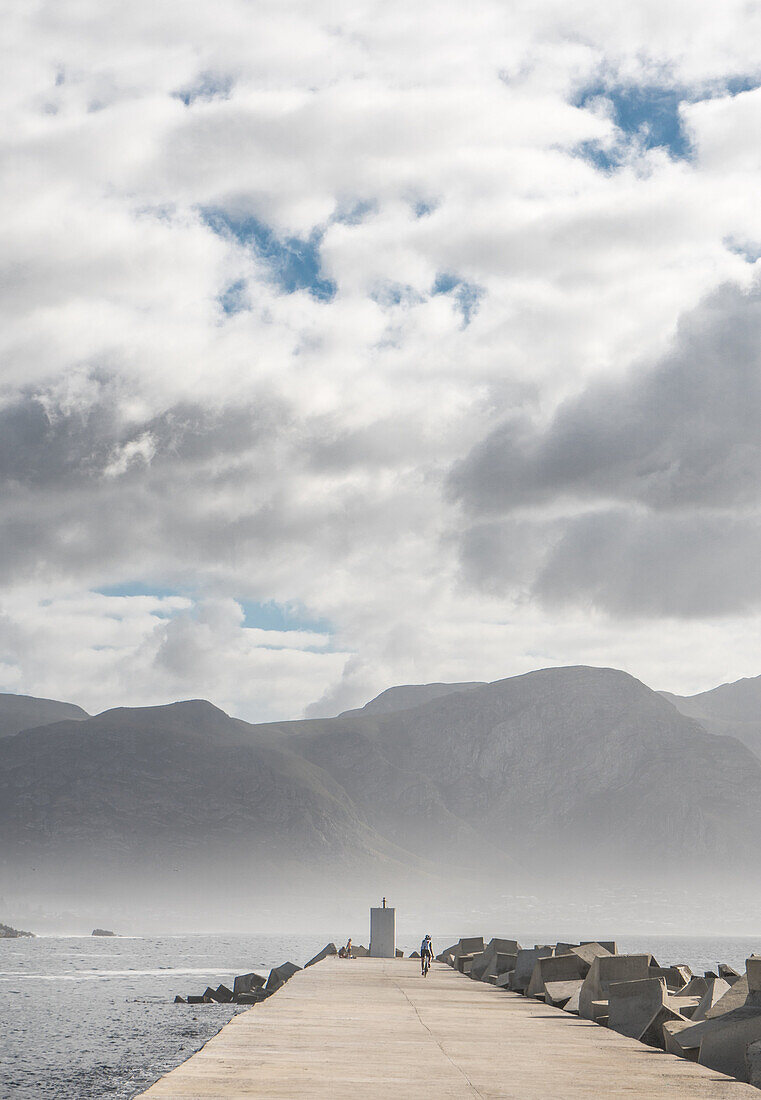 Als Sonne bricht am frühen Morgen Nebel, Radfahrer am Ende der Pier, New Harbor, Hermanus, Südafrika, Afrika