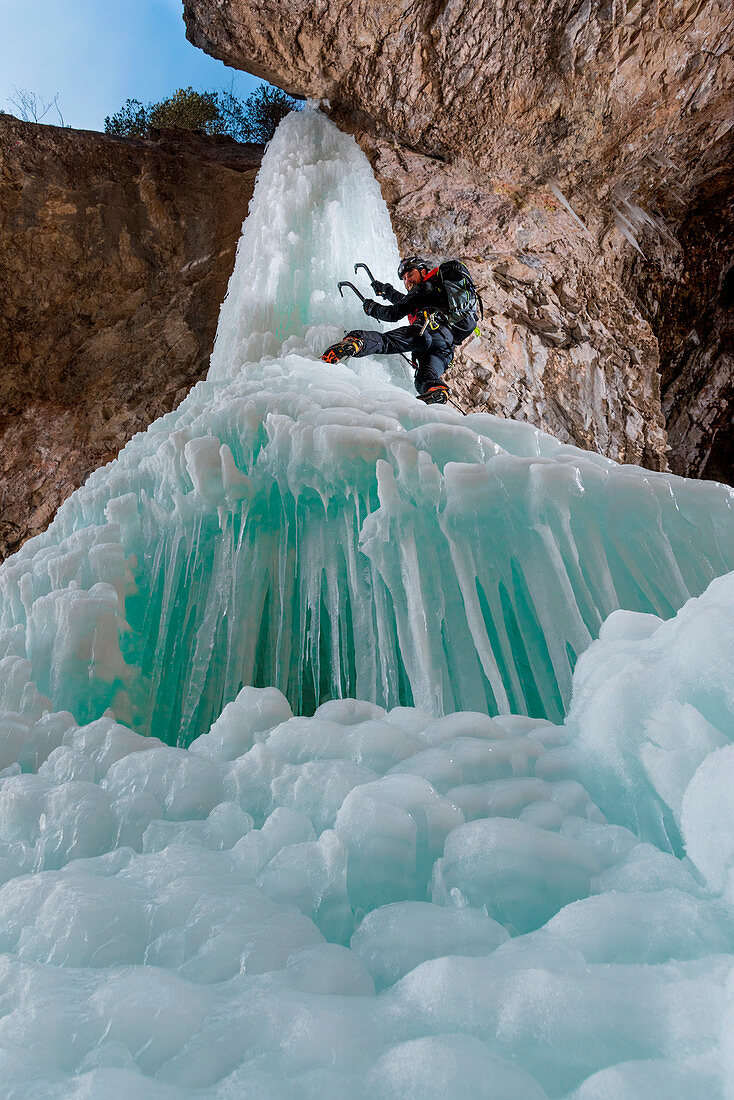 Eis-Kaskaden, ein Mann klettert mit einer Eispickel, Block von gefrorenem Eis in den europäischen Alpen, Dolomiten, Fassatal, Italien, Europa, Trentino, Alpen