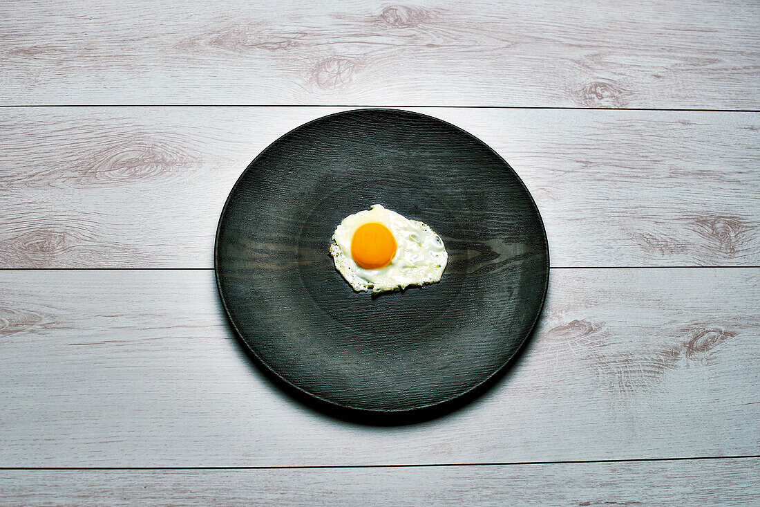 Top view of an egg and a black dish on a white wooden table