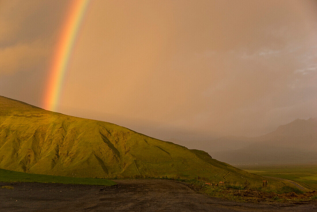 Ein Regenbogen, der im Licht des Sonnenuntergangs gebildet wurde, nach einem starken Sturm kommt aus den grünen Bergen an der Küste Dyhrolaey, Island