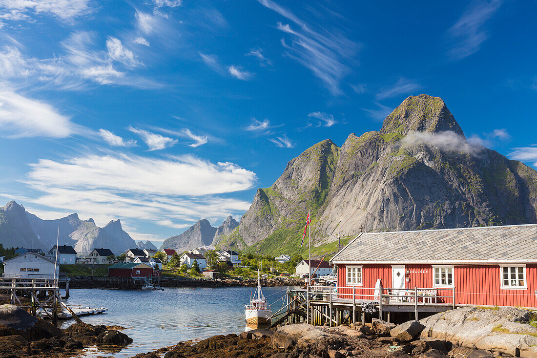 Typisches Haus der Fischer genannt Rorbu umrahmt von felsigen Gipfeln und blauen Meer Reine Moskenes Lofoten Inseln Norwegen Europa