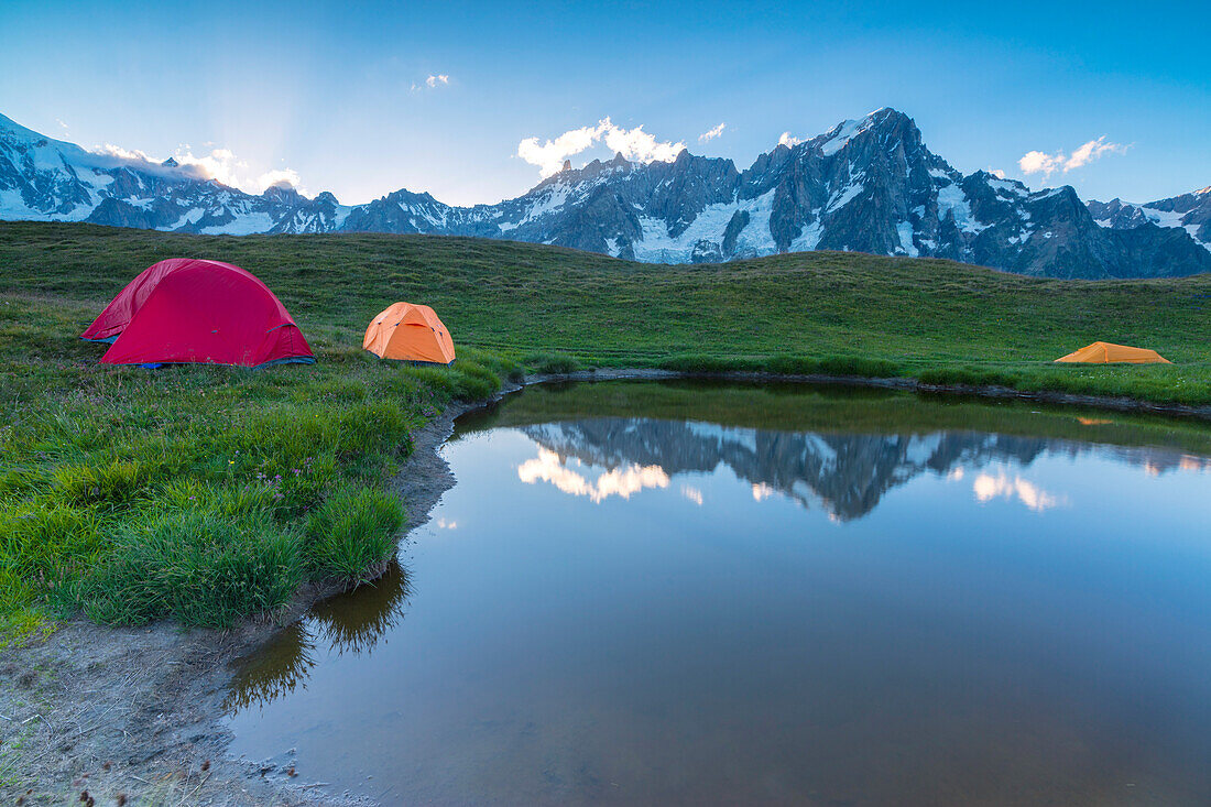 Camping tents in the green meadows surrounded by alpine lake at dusk Mont De La Saxe Courmayeur Aosta Valley Italy Europe