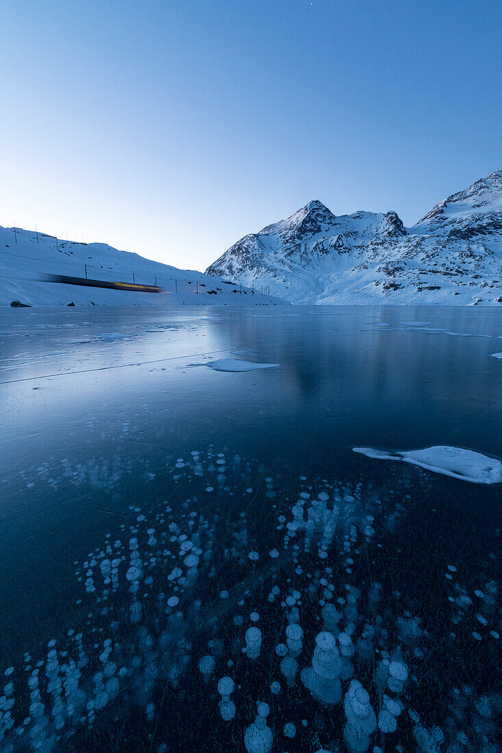 Ice bubbles frame the snowy peaks reflected in Lago Bianco Bernina Pass canton of  Graubünden Engadine Switzerland Europe