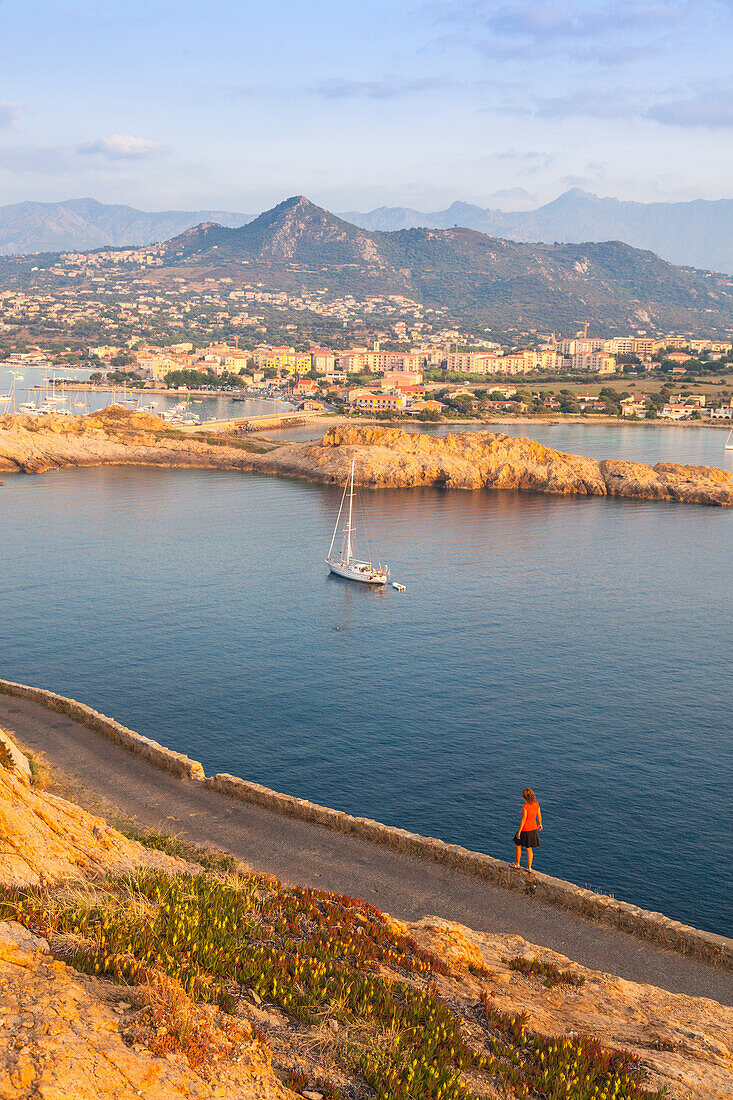 Tourist auf einer Straße bewundert das Segelboot im klaren Meer um das Dorf Ile Rousse Balagne Region Korsika Frankreich Europa