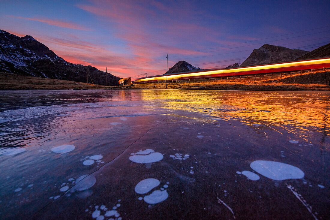 Bernina Express train next to the frozen Lake Pitschen at sunset Bernina Pass Canton of Graubünden Engadine Switzerland Europe