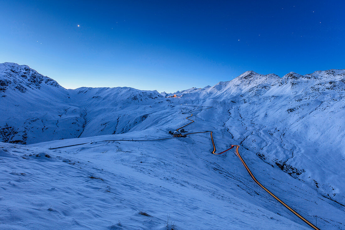 Blaues Licht der Dämmerung auf der verschneiten Landschaft und die Haarnadelkurven des Stelvio Passes Braulio Tal Valtellina Lombardei Italien Europa