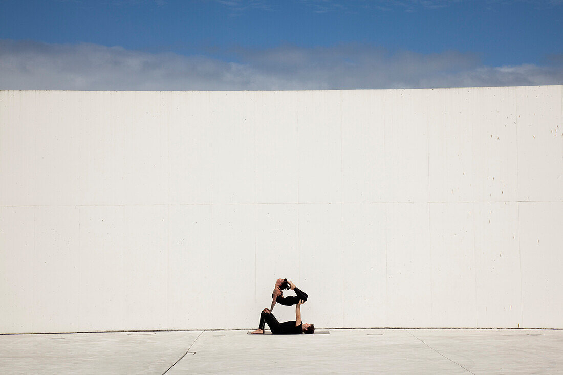 Adult Man Balancing Adult Frau während Yoga Pose mit großen weißen Wand im Hintergrund