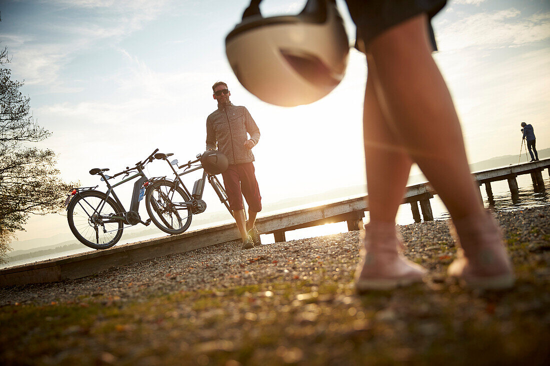 man and woman with eBike and helmets near the lakeshore, Lake Starnberg, Upper Bavaria, Germany