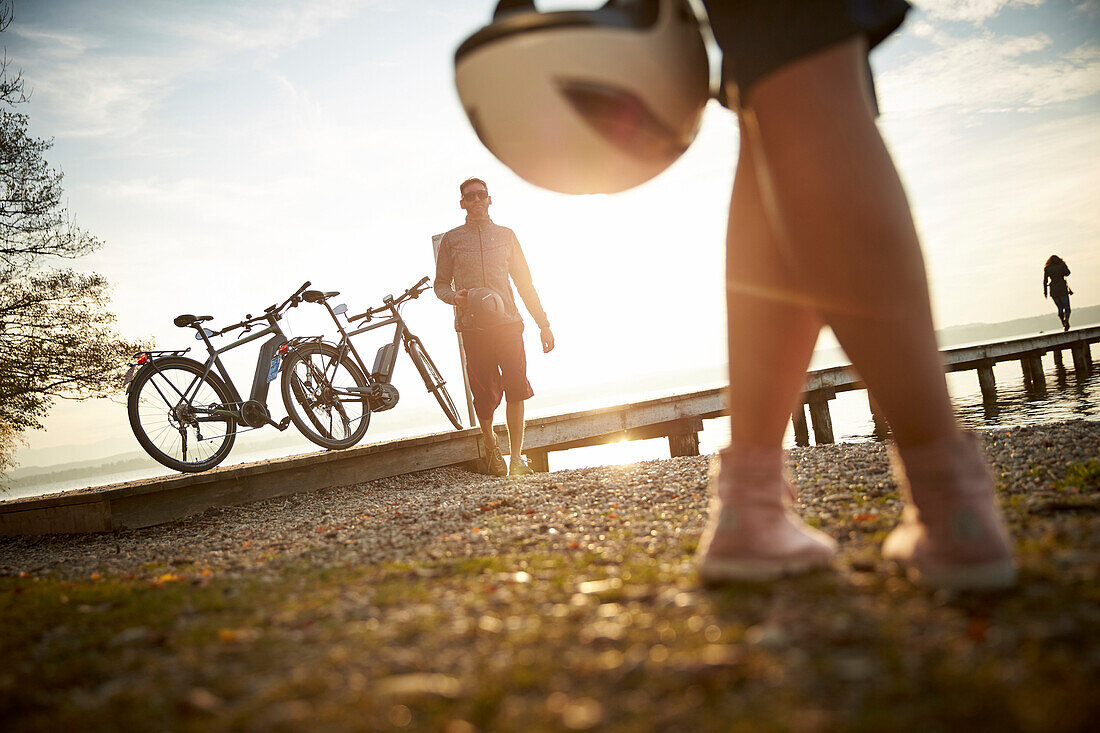 man and woman with eBike and helmets near the lakeshore, Lake Starnberg, Upper Bavaria, Germany