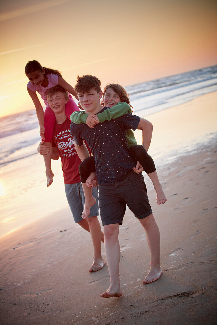 2 Mädchen werden von Ihren grossen Brüdern über den Strand getragen, Abends , Playa da Roche Andalusien, Südwestküste Spanien, Atlantik, Europa