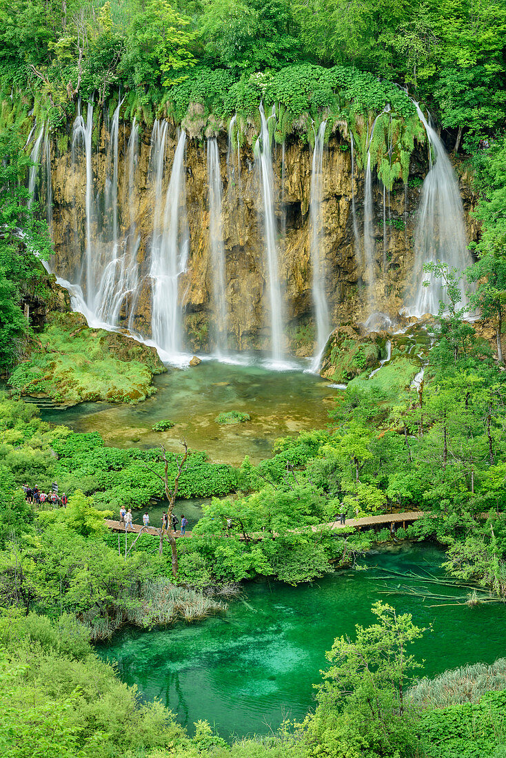 Personen wandern auf Steg an See und Wasserfall von Plitvitz vorbei, Plitvitzer Seen, Nationalpark Plitvitzer Seen, Plitvice, UNESCO Weltnaturerbe Nationalpark Plitvitzer Seen, Kroatien