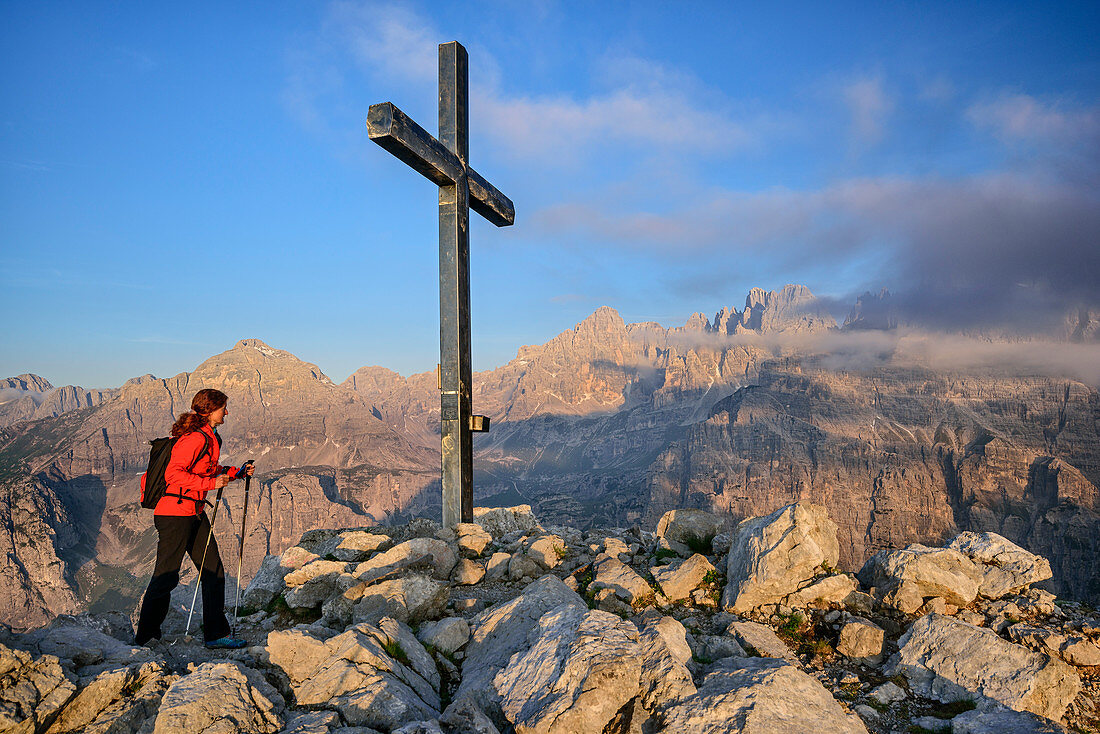 Woman hiking ascending towards cross at summit, Brenta group in background, Croz dell' Altissimo, Brenta group, UNESCO world heritage site Dolomites, Trentino, Italy