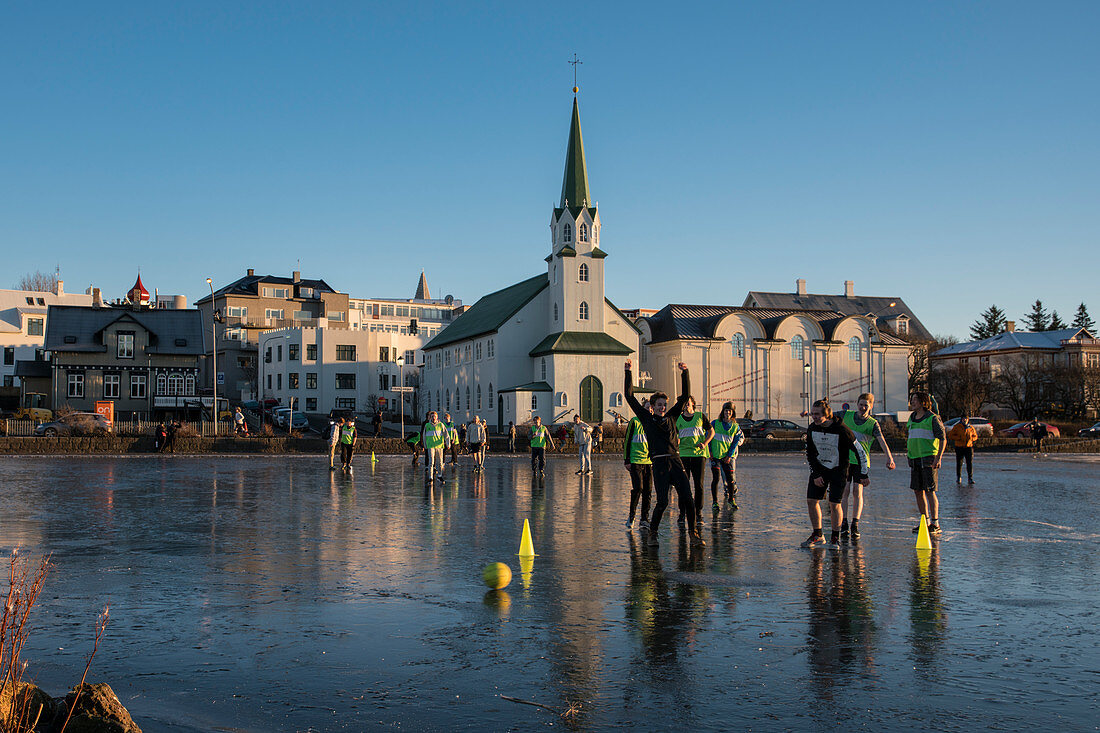Schüler spielen auf dem zugefrorenen Tjörnin See Fußball mit der Fríkirkjan (Frikirkjan) Kirche dahinter, Reykjavik, Island, Iceland, Europa