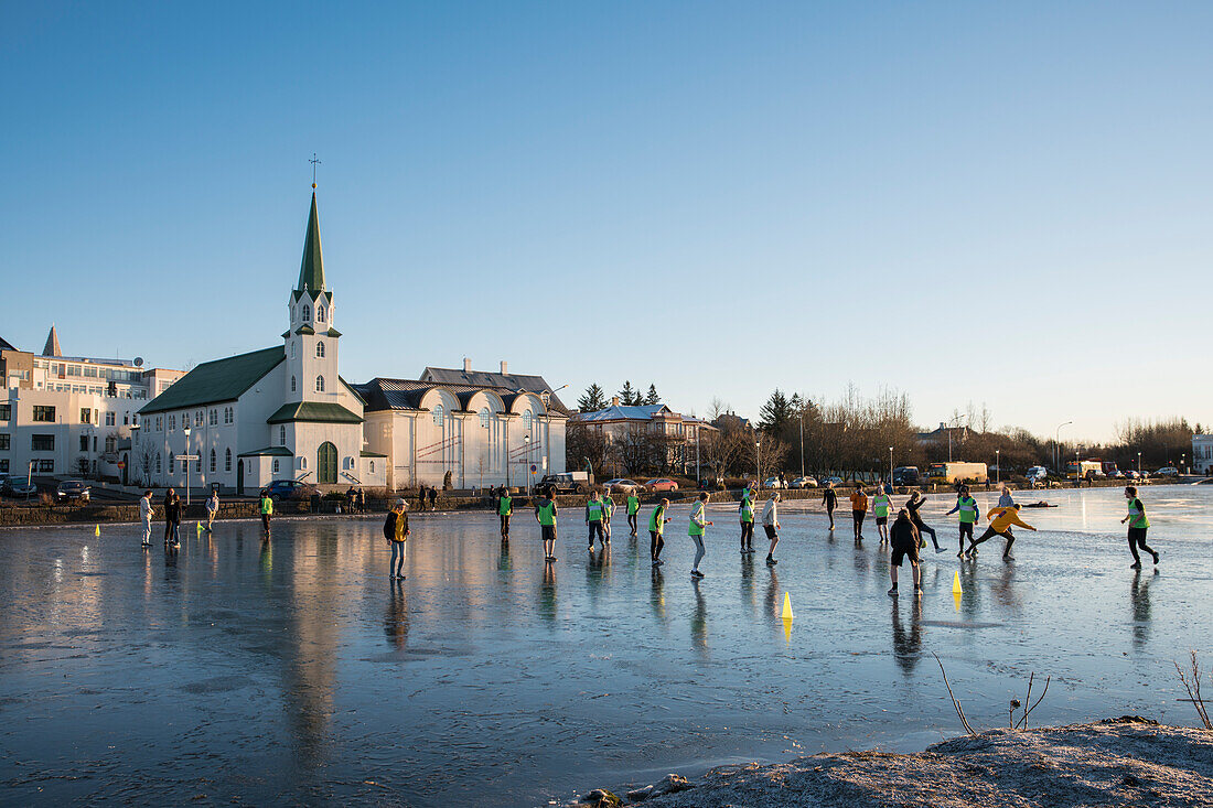 School children play soccer on frozen Tjörnin lake with Fríkirkjan (Frikirkjan) church behind, Reykjavik, Iceland, Europe