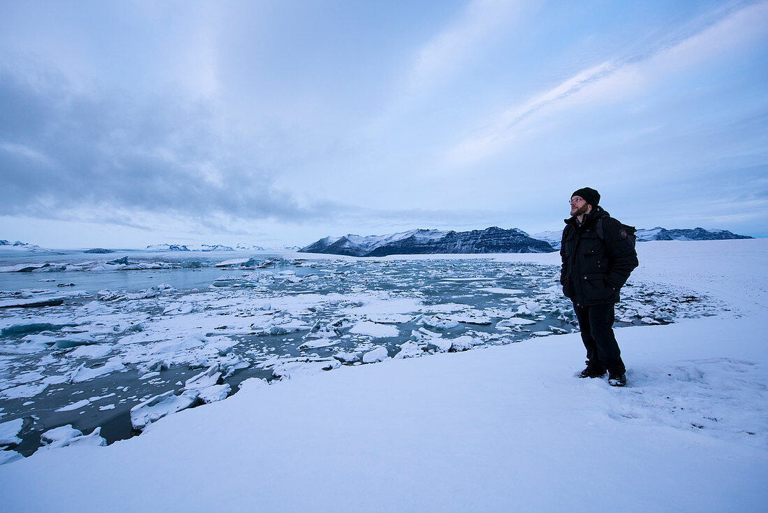 Man overlooks Jökulsárlón (Jokulsarlon) Glacier Lagoon in snowy winter landscape during the last light of the day, Jökulsárlón (Jokulsarlon), Iceland, Europe