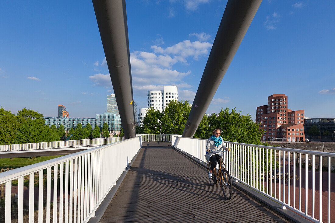 Radfahrerin auf einer Brücke über den Medienhafen, Blick zum Neuen Zollhof von Frank O. Gehry, Düsseldorf, Nordrhein-Westfalen, Deutschland