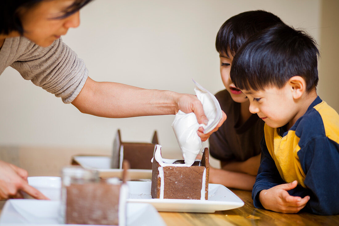 A Japanese American mother helps put together a Gingerbread house at Christmastime with her two Japanese American sons with whom the younger is four years old and the older is is 7 years old.