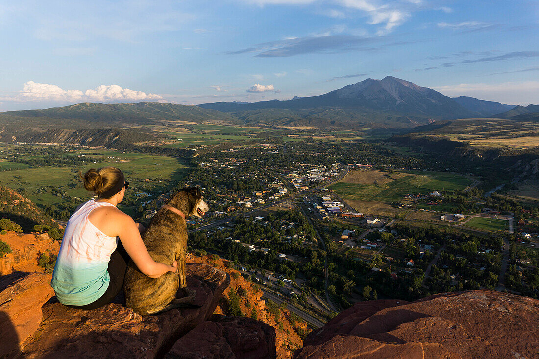 Young female and her dog overlooking a mountain and town at sunset