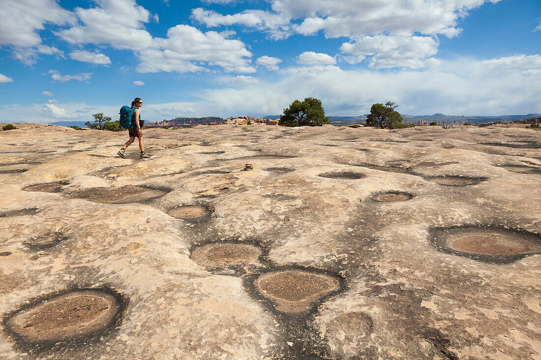 A woman walks past sandstone potholes on the trail to the Confluence Overlook in Canyonlands National Park, Utah.