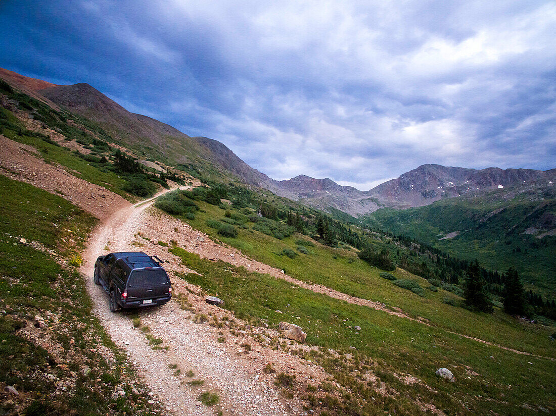Aerial view of a truck driving up a rocky mountain pass road with a cloudy sky