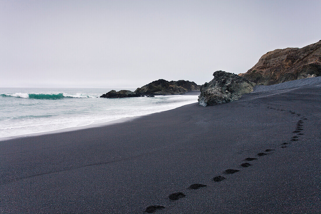 Footsteps left in the black sand beach of Shelter Cove, CA