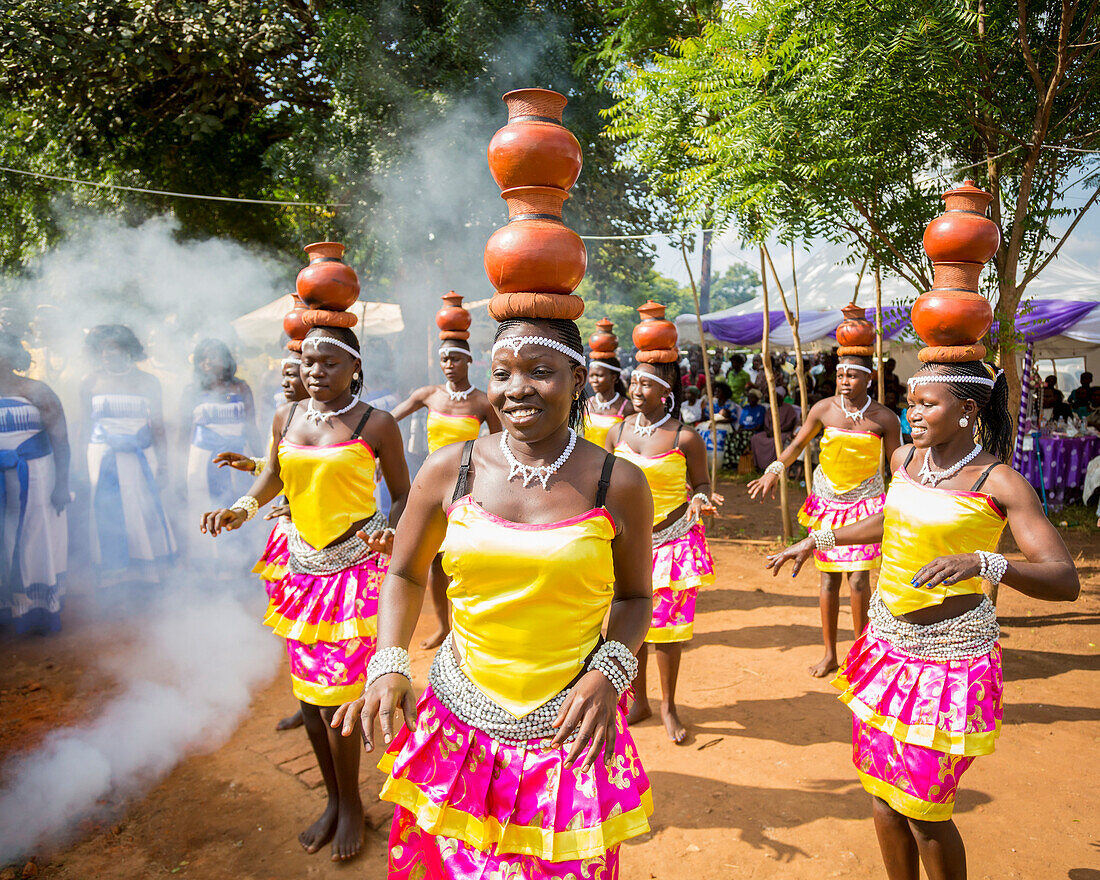 'Frauen, die eine farbenfrohe, traditionelle Kleidung tragen und die Töpferei auf dem Kopf tragen; Uganda'
