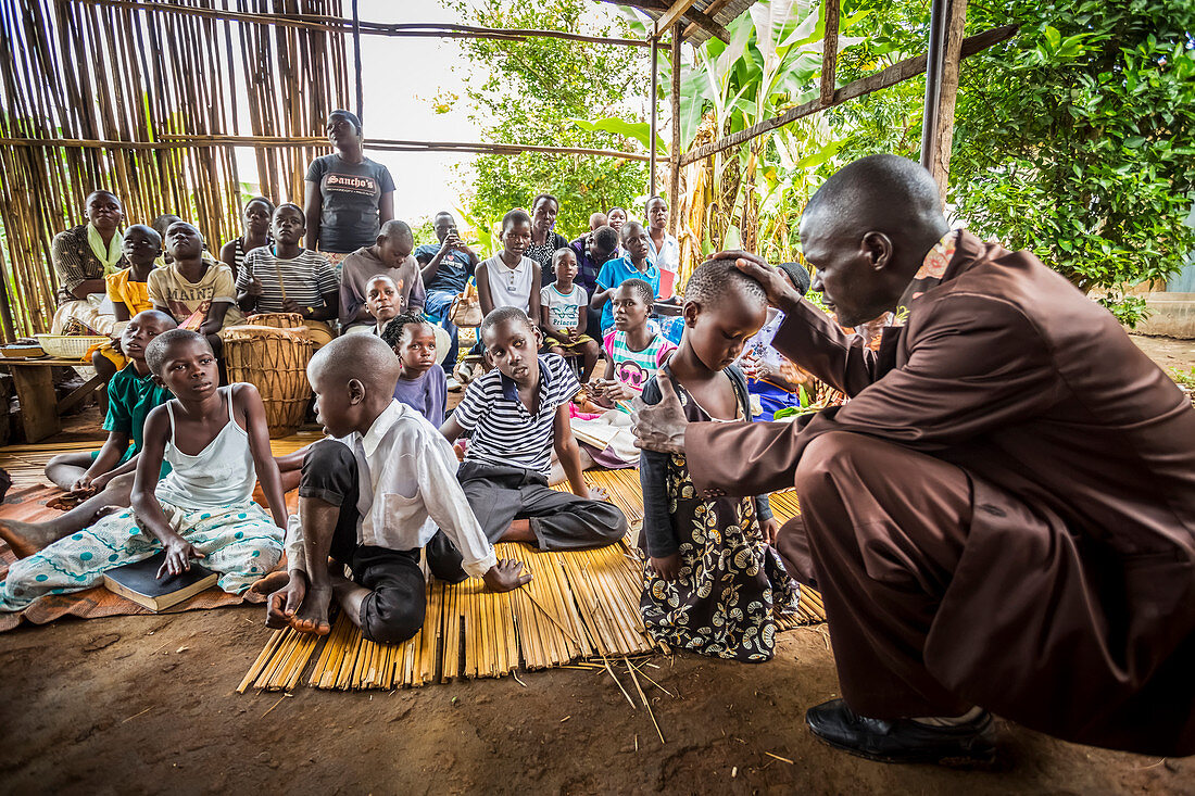 'Ein Pfarrer betet für ein kleines Kind; Gulu, Uganda'