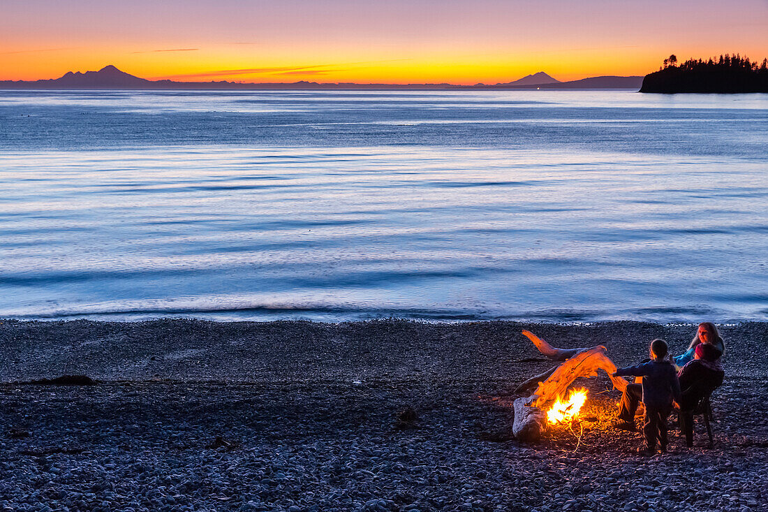 Menschen genießen ein Lagerfeuer am Strand bei Sonnenuntergang, Hesketh Island, South Central Alaska, USA