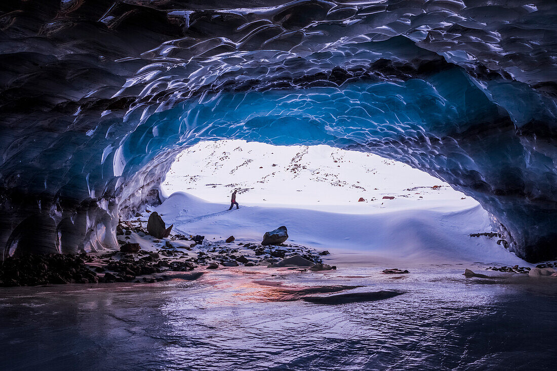 Ein Mann wird von dem Eingang zu einer großen Eishöhle in der Nähe der Endstation des Augustana Gletschers in der Alaska Range im Winter umrahmt. Alaska, Vereinigte Staaten von Amerika