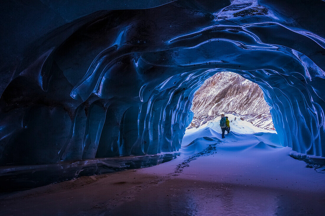 'A hiker exits a small ice cave while exploring the terminal moraine of Black Rapids Glacier in the winter; Alaska, United States of America'